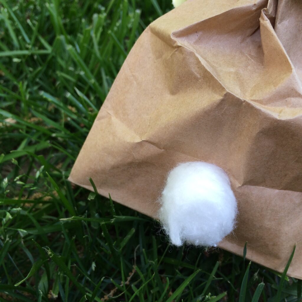 Zoomed in view of brown paper lunch bag near bottom where cotton ball has been added for a bunny tail. 